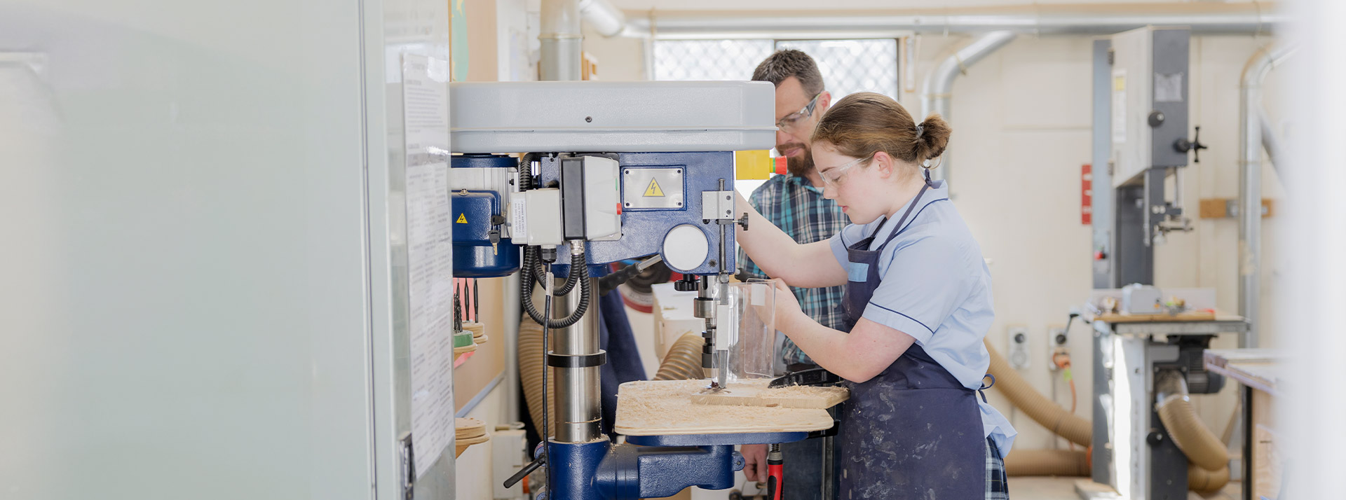A teacher and his student using machinery in the workshop at St Columba’s Catholic College Springwood
