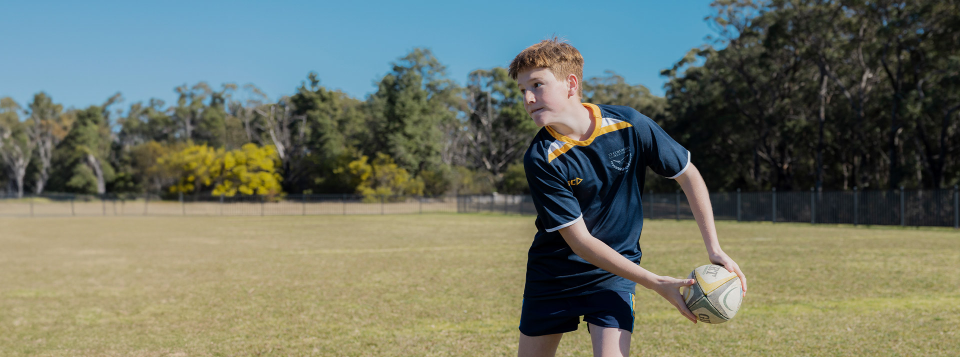 Student playing football on the school oval at St Columba’s Catholic College Springwood