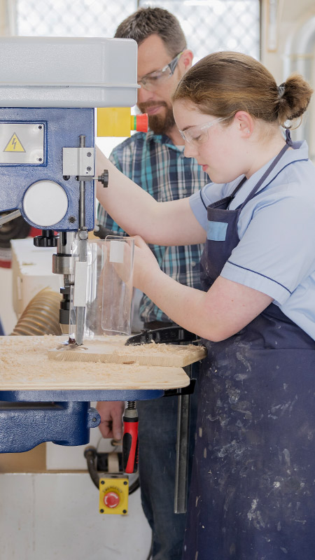 A teacher and his student using machinery in the workshop at St Columba’s Catholic College Springwood