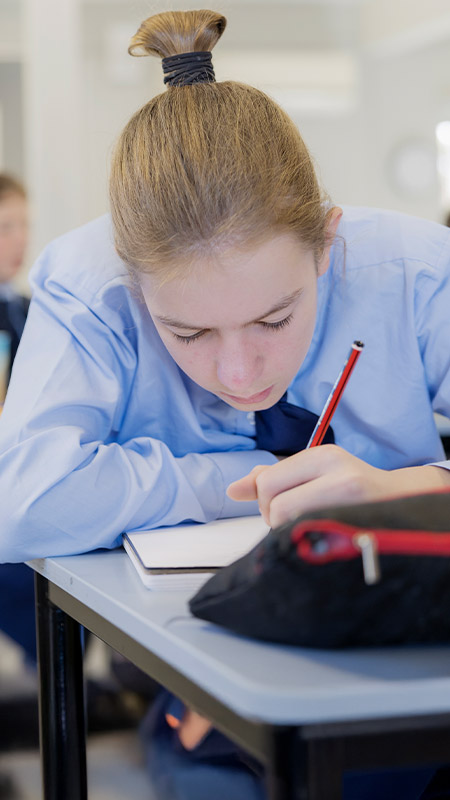 Student writing in her workbook in the classroom at St Columba’s Catholic College Springwood