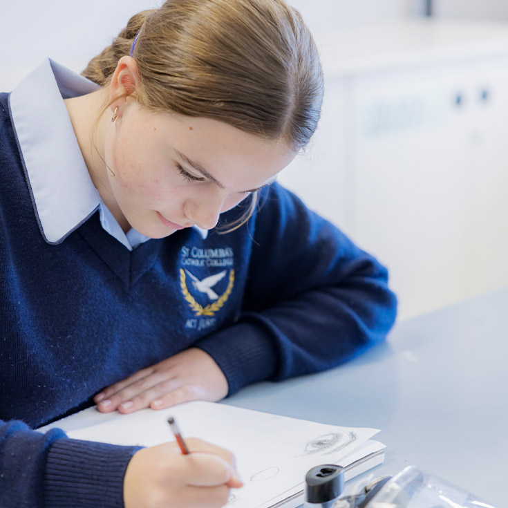 Student writing at her desk in the classroom at St Columba’s Catholic College Springwood