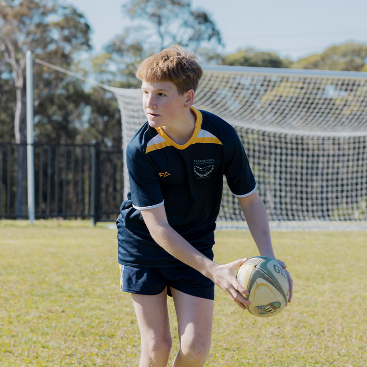 Student playing football on the school oval at St Columba’s Catholic College Springwood